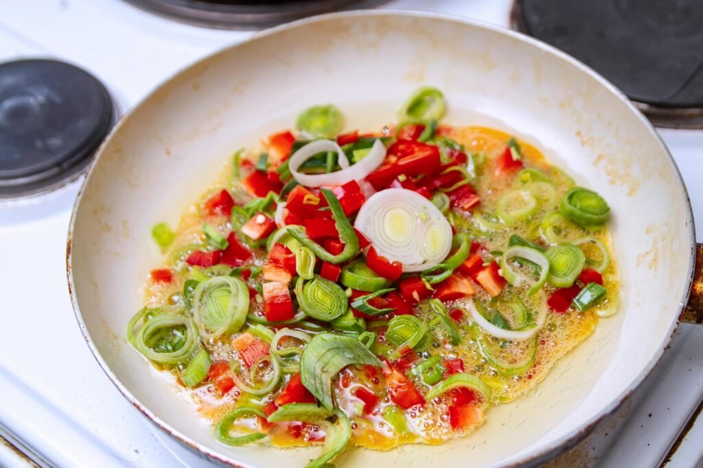 Bright vegetables cooking in oil on a stovetop.